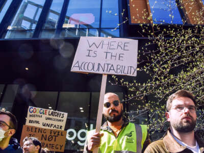 A protester in a yellow vest holds a sign reading "WHERE IS THE ACCOUNTABILITY" during an outdoor protest