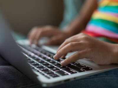 Youth with rainbow striped shirt types on laptop, close-up on hands on keys