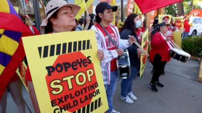 Fast food worker holds up sign saying "Popeyes, stop exploiting child labor" at protest