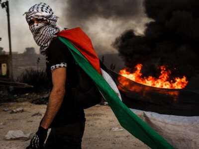 A Palestinian dons a Palestinian flag during while protesting the Israeli occupation in the West Bank, as protesters are met with tear gas, flashbangs and live fire from Israeli forces, in Ramallah, Palestine, on October 13, 2023.