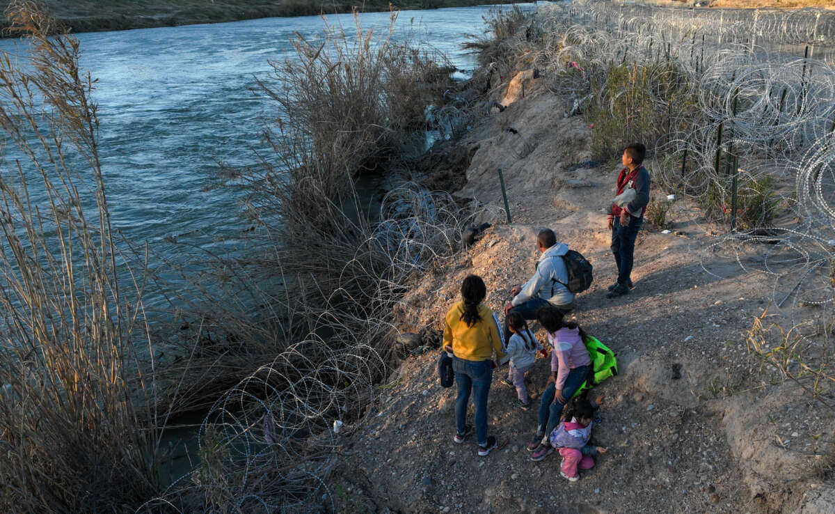 An aerial view shows migrants, including children, walking next to razor wire after crossing the Rio Grande to seek humanitarian asylum during sunset in Eagle Pass, Texas, on February 4, 2024.