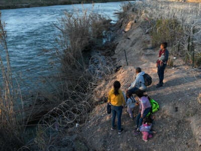 An aerial view shows migrants, including children, walking next to razor wire after crossing the Rio Grande to seek humanitarian asylum during sunset in Eagle Pass, Texas, on February 4, 2024.