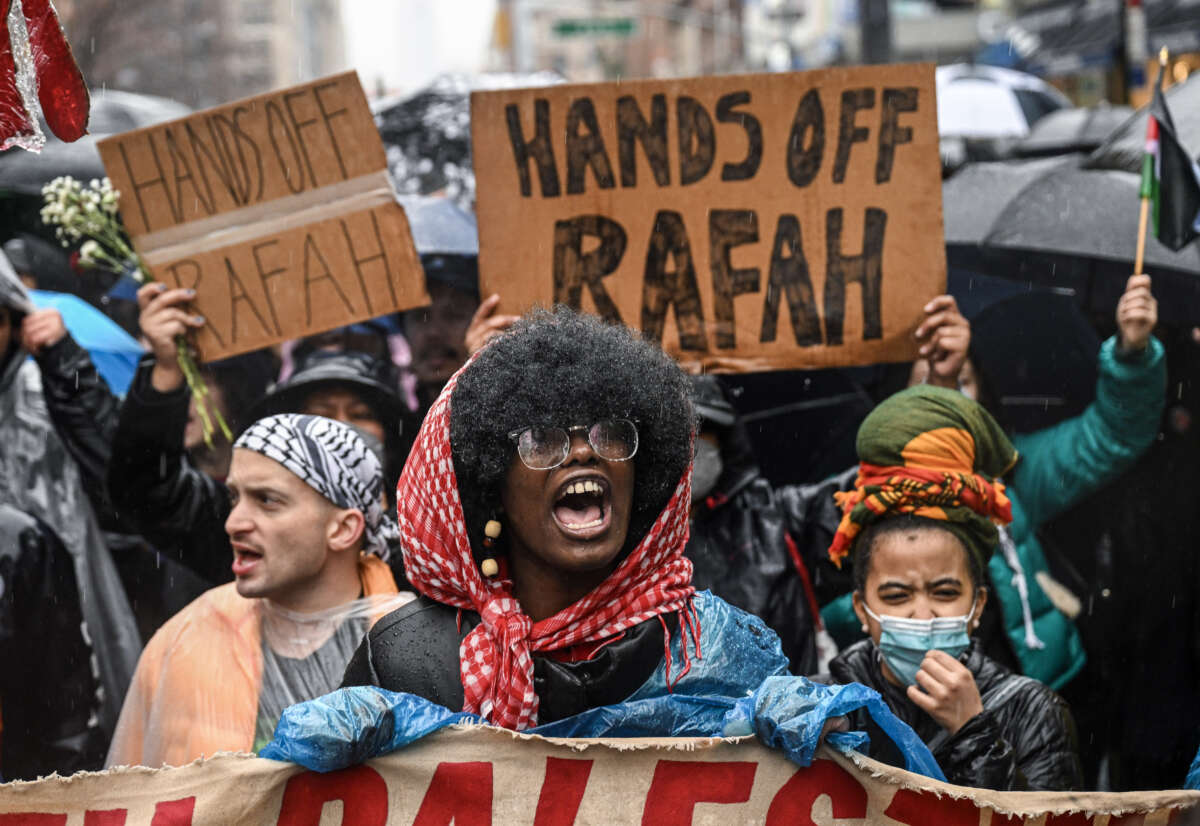 Pro- Palestine protesters wearing keffiyehs hold signs saying "Hands off Rafah" at a protest in the pouring rain