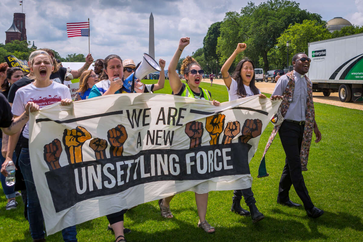 People march behind a banner reading "WE ARE A NEW UNSETTLING FORCE" during an outdoor rally