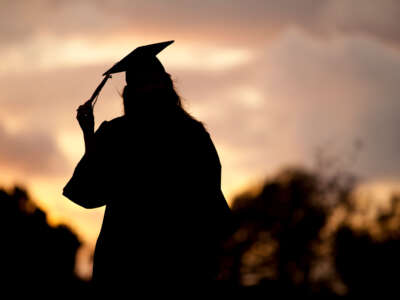 College graduate adjusts tassel on cap, in silhouette