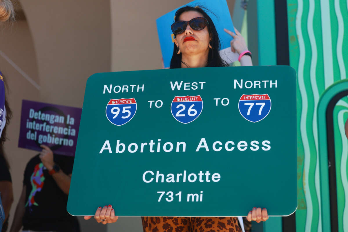 A protester holds a sign displaying different highway routes to get reproductive care during an outdoor protest