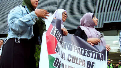 Three women in hijabs hold a banner reading "Free Palestine from the guilt of Germany" during an outdoor protest