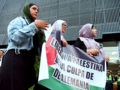 Three women in hijabs hold a banner reading "Free Palestine from the guilt of Germany" during an outdoor protest