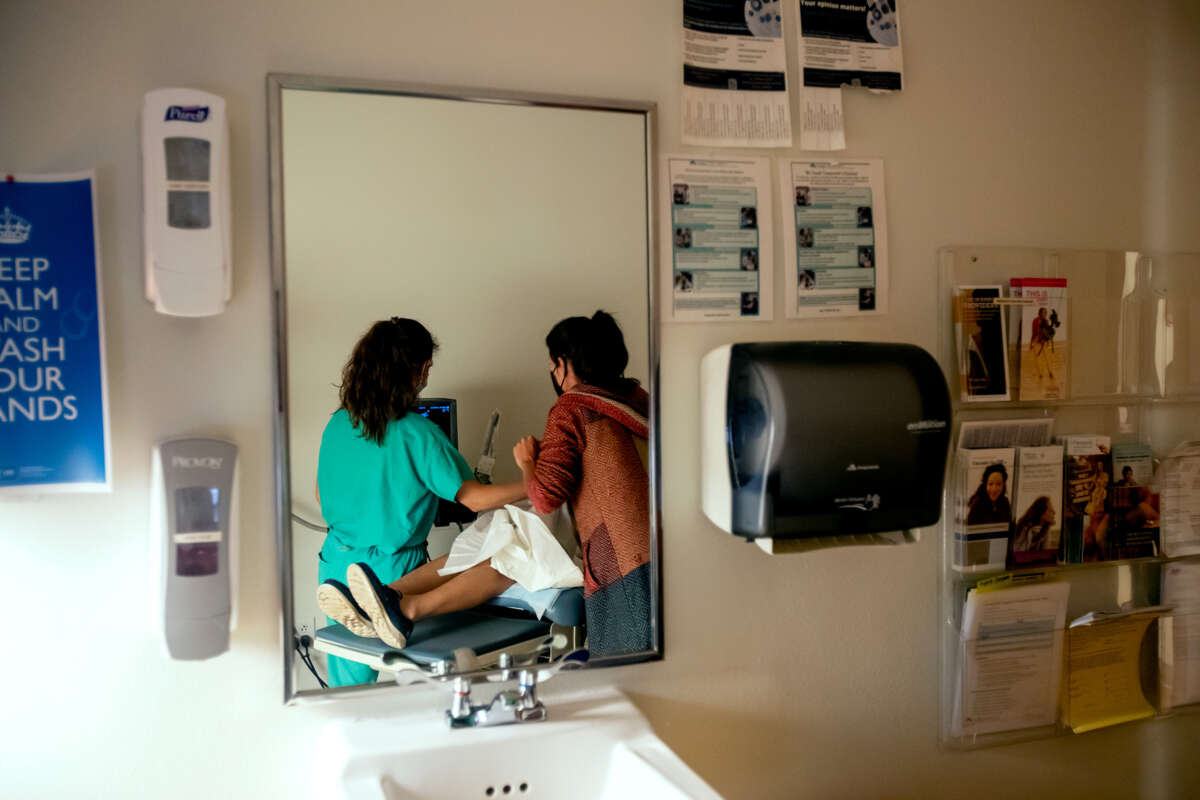 A patient recieves care from two medical professionals, as seen through a mirror reflecting them from behind