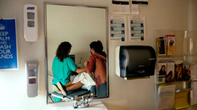 A patient recieves care from two medical professionals, as seen through a mirror reflecting them from behind