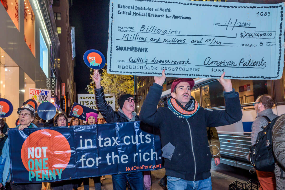A protester holds up an oversized prop check made out to "billionaires" to the tune of "millions and millions" and signed for by "American Patients" during an outdoor protest