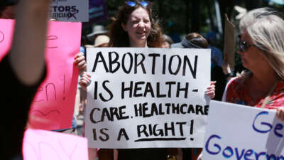A protester holds a sign reading "ABORTION IS HEALTHCARE. HEALTHCARE IS A RIGHT" during ano outdoor protest