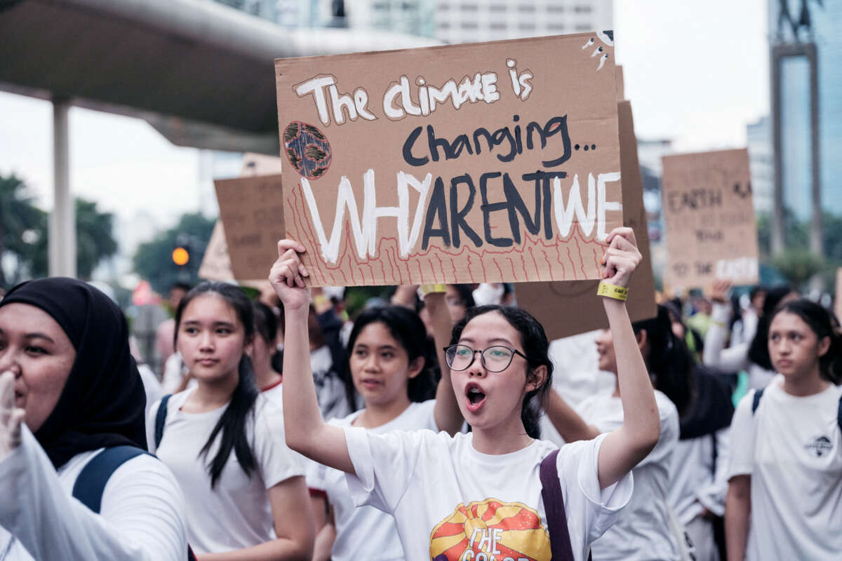 A chanting protester holds a sign reading "THE CLIMATE IS CHANGING: WHY AREN'T WE" during an outdoor protest