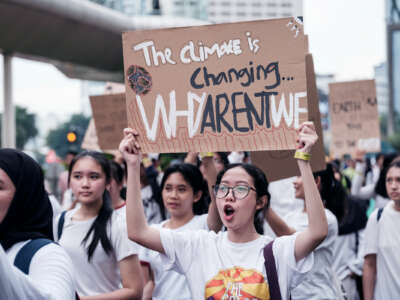 A chanting protester holds a sign reading "THE CLIMATE IS CHANGING: WHY AREN'T WE" during an outdoor protest