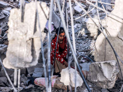A Palestinian girl among rubble, as seen from behind rebar that lends itself to making her look imprisoned