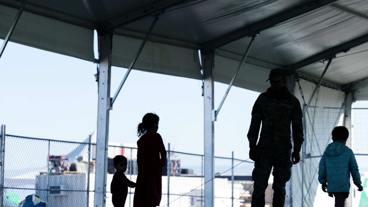 Silhouettes of children are seen beside an adult troop at a refugee camp