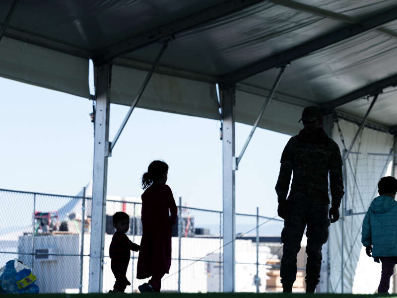 Silhouettes of children are seen beside an adult troop at a refugee camp