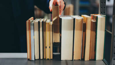 Person sets book down between other books at library