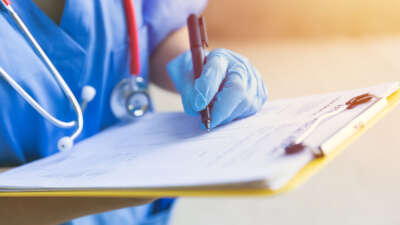 Medical worker with stethoscope writing on clipboard, close angle on hand with pen.