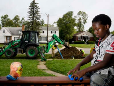 Kane Watkins, 9, sits on the edge of his porch playing with toys as crews work to inspect his homes water line as part of the lead line replacement program on August 12, 2021, in Flint, Michigan.