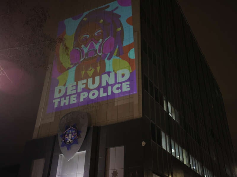 A protester projects ''Defund The Police'' on the wall of the Oakland Police Department as people gather at the Frank H. Ogawa Plaza following the police-perpetrated killing of Tyre Nichols by Memphis police, in Oakland, California, on January 29, 2023.