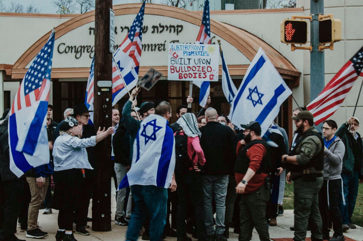 Zionists encircle anti-Zionist protesters standing with keffiyehs and a sign reading "Waterfront properties built upon bulldozed bodies" outside of Shomrei Emunah in Baltimore, Maryland.