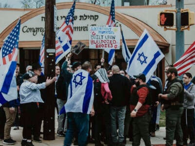 Zionists encircle anti-Zionist protesters standing with keffiyehs and a sign reading "Waterfront properties built upon bulldozed bodies" outside of Shomrei Emunah in Baltimore, Maryland.