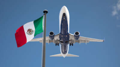 A plane flies overhead past a Mexican flag