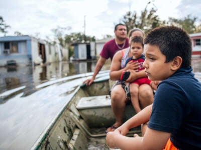 A kid looks out sadly at his flooded neighborhood as he sits in a canoe with his family
