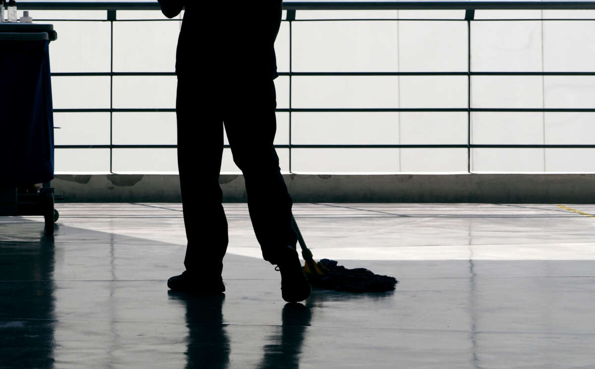 A janitor cleans a floor with a mop, in silhouette.