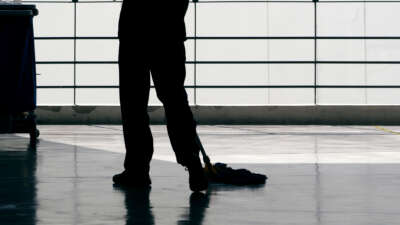 A janitor cleans a floor with a mop, in silhouette.