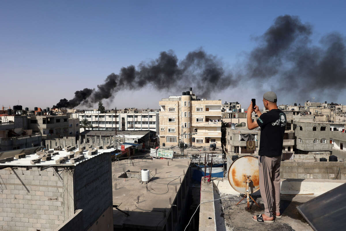 A man snaps pictures from a rooftop as thick, black smoke rises from a fire in a building caused by Israeli bombardment in Rafah in the southern Gaza Strip on May 10, 2024.