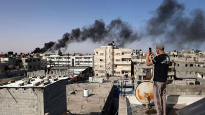 A man snaps pictures from a rooftop as thick, black smoke rises from a fire in a building caused by Israeli bombardment in Rafah in the southern Gaza Strip on May 10, 2024.