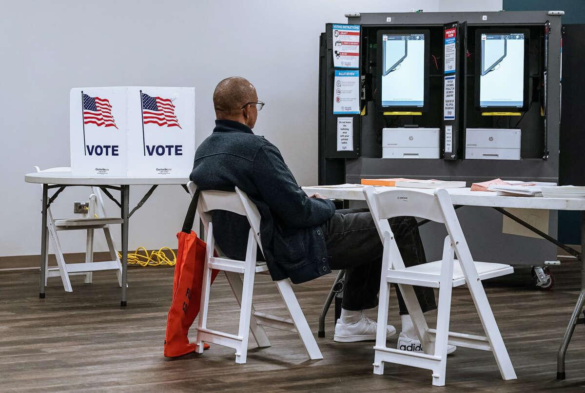 A man sits at a desk near several voting kiosks