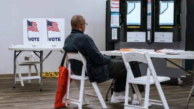 A man sits at a desk near several voting kiosks