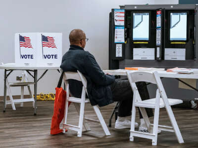 A man sits at a desk near several voting kiosks