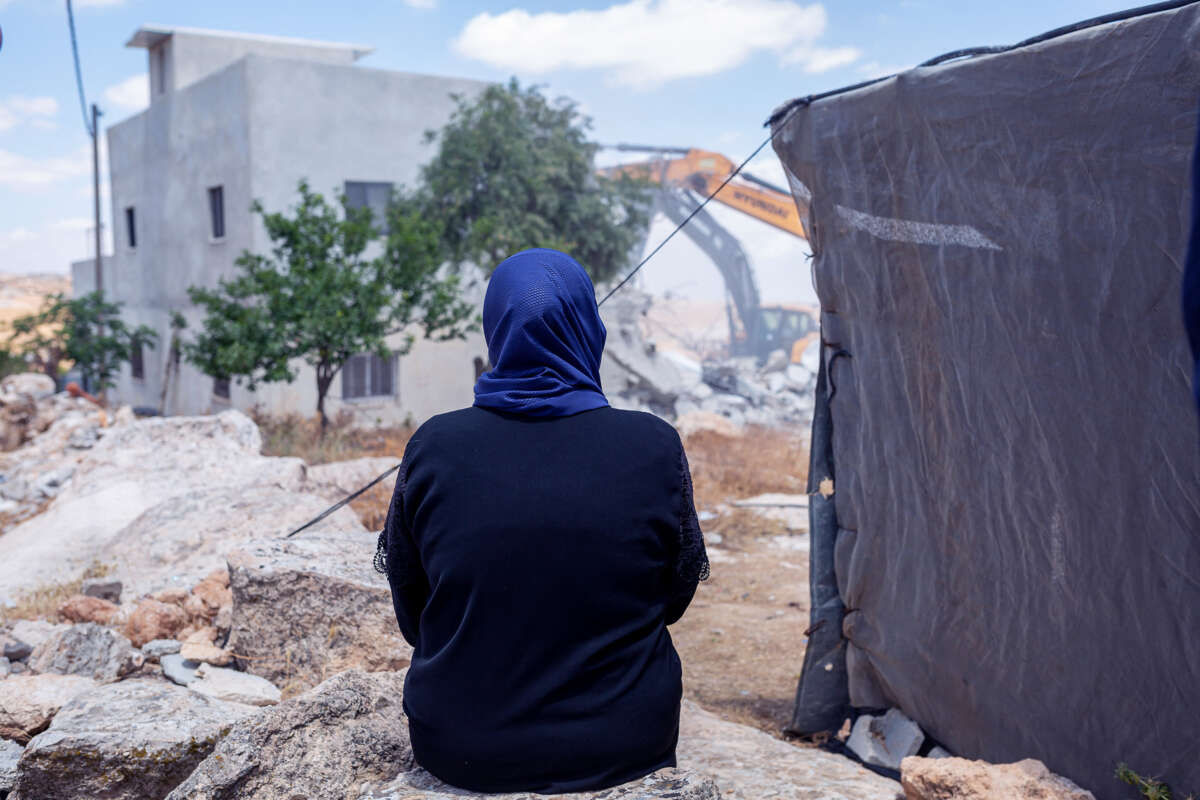 A woman in a blue hijab watches Israeli forces tear down her home