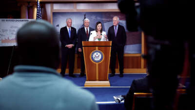 Katie Britt speaks at a podium as Mitch Mcconnell and two other republicans stand behind her