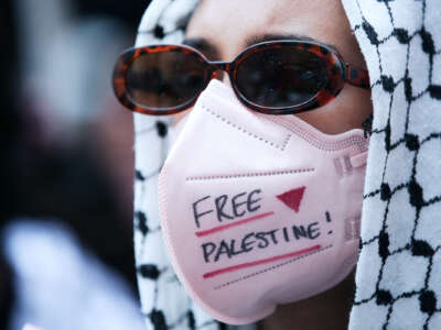 A protester with a medical mask reading "FREE PALESTINE" participates in an outdoor protest