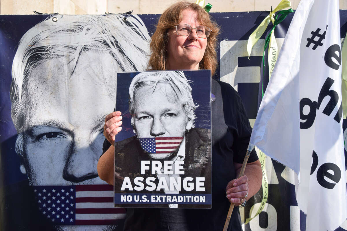 A woman holds a sign bearing Julian Assange's face being gagged with a U.S. flag above the words "FREE ASSANGE; NO U.S. EXTRADITION" during an outdoor protest