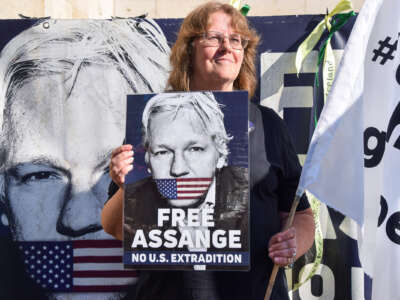 A woman holds a sign bearing Julian Assange's face being gagged with a U.S. flag above the words "FREE ASSANGE; NO U.S. EXTRADITION" during an outdoor protest
