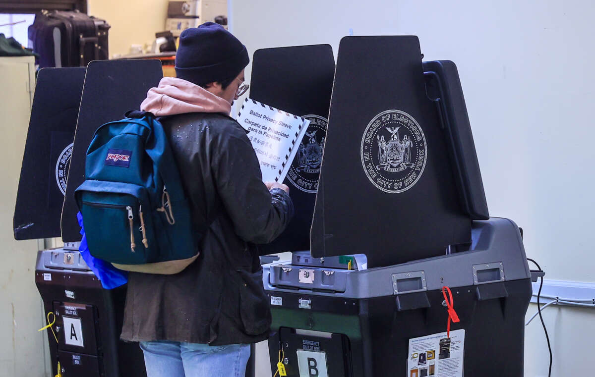 A voter wearing a beanie and a backpack stands at a booth in preparation to vote