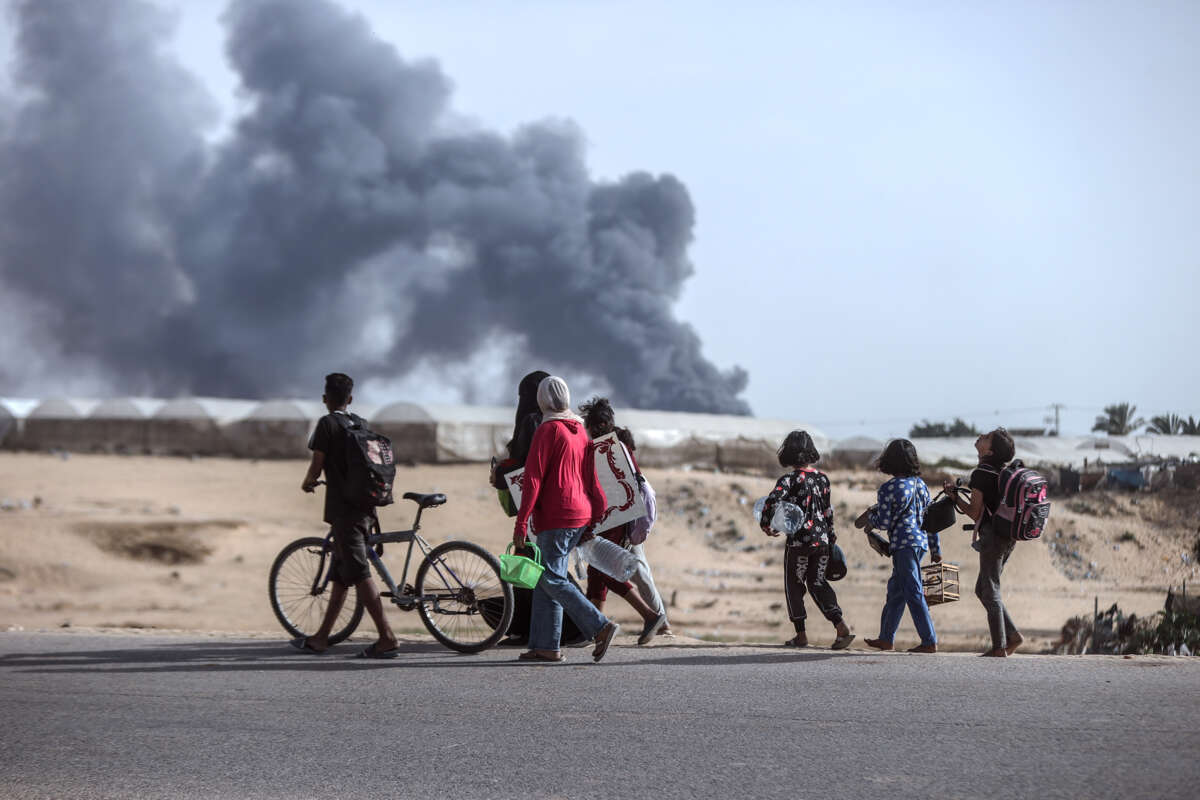 People walk by the tent cities of a refugee camp as smoke rises from where they were bombed