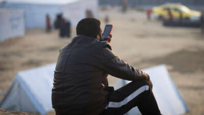 A displaced Palestinian man uses the phone in a refugee camp