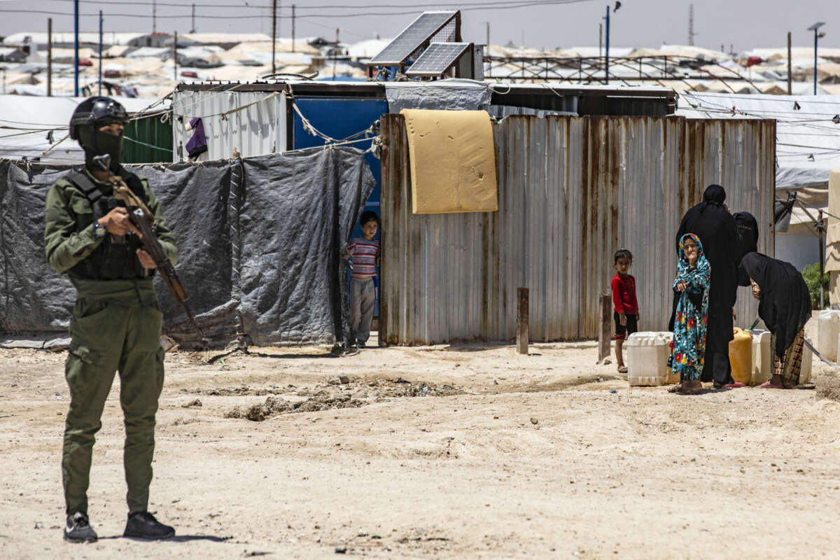 A member of the Kurdish security forces stands guard as women and children fill water containers at the Al-Hol camp in Syria's northeastern Al-Hasakah Governorate, on October 10, 2023.