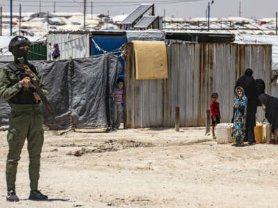 A member of the Kurdish security forces stands guard as women and children fill water containers at the Al-Hol camp in Syria's northeastern Al-Hasakah Governorate, on October 10, 2023.