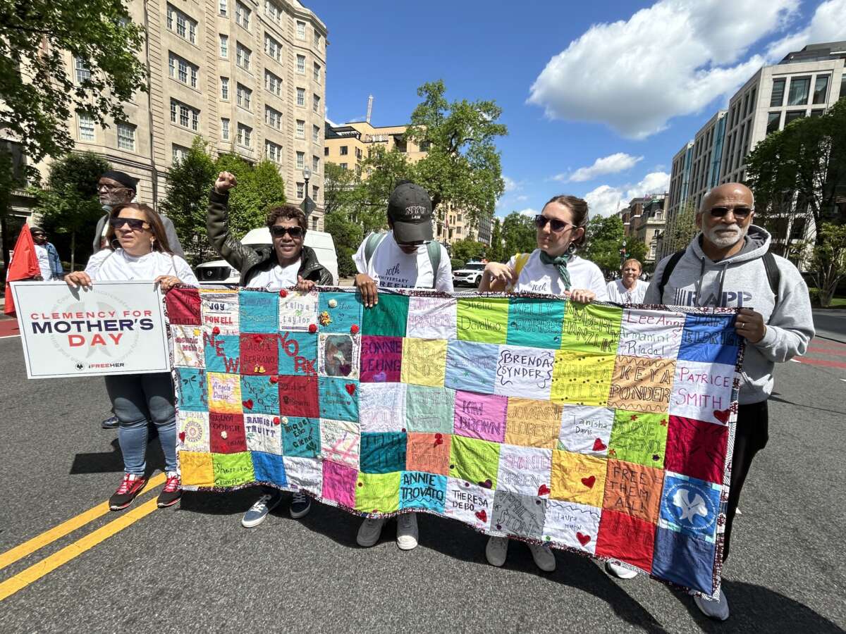 Formerly incarcerated New Yorkers holding a quilt with names of those seeking clemency.