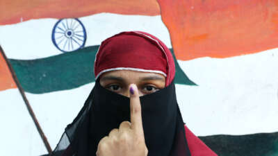 A Muslim voter holds up her finger, inked to denote that she's voted, while standing in front of a mural showing the Indian flag