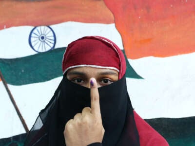 A Muslim voter holds up her finger, inked to denote that she's voted, while standing in front of a mural showing the Indian flag