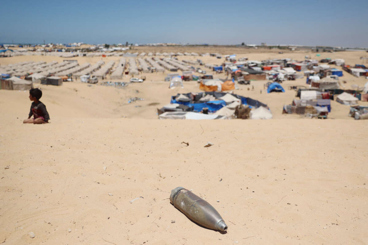 A child plays on a sand dune next to an unexploded ordnance, in view of the tent city in Rafah